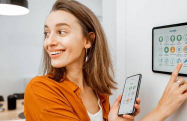 A woman smiling while using a tablet in the wall and holding a smart phone